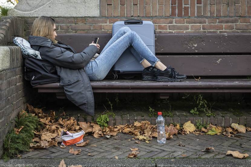 Jonger zonder vaste woon- of verblijfplaats in Amsterdam buiten op een bankje met een koffer